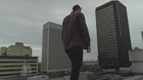 Caucasian-man-walking-along-a-rooftop-in-a-city-during-a-cloudy-day