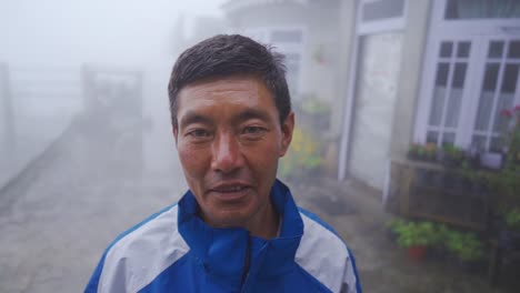 Alone-old-Asian-man-looks-at-camera-and-smiles-on-misty-and-foggy-morning-at-hill-station