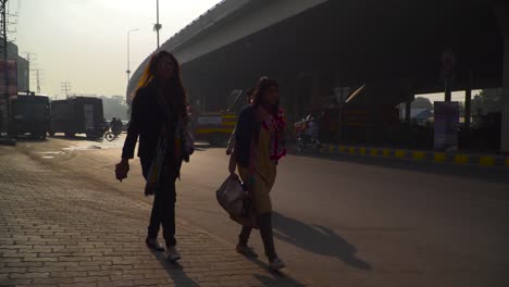 Traffic-on-the-road-under-the-fly-over,-A-couple-of-girls-with-having-mobile-phone-in-her-hand-are-coming-from-the-foot-path,-Rescue-and-emergency-vans-crossing-the-roads