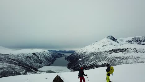 Drohnen-Luftaufnahmen-Von-Zwei-Skifahrern,-Die-Den-Gipfel-Des-Berges-Besteigen,-Mit-Atemberaubender-Aussicht-Auf-Die-Berge-Nordnorwegens-Und-Das-Arktische-Meer