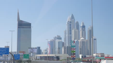 Conduciendo-Por-Una-Calle-De-Dubai-Junto-Al-Puerto-Deportivo-De-Dubai-Y-Enormes-Rascacielos