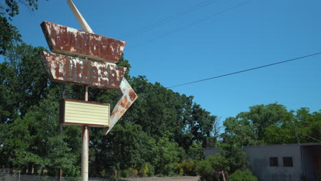 Rotating-right-pan-shot-of-a-rusty-retro-store-sign-out-front-of-an-abandoned-lumber-yard-on-a-bright-sunny-day