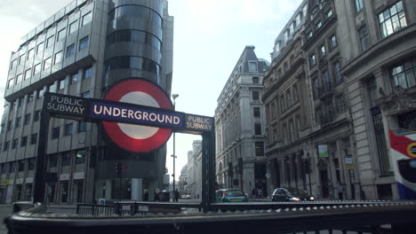 Buses-traveling-down-the-road-next-to-a-London-Underground-entrance-in-London,-England
