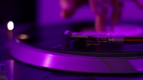 A-record-player-needle-spins-under-the-purple-and-pink-colored-lights-of-a-DJ-light-sound-and-smoke-set-up