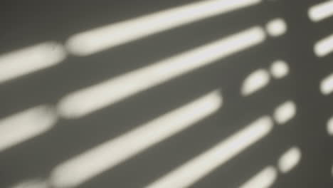 Man-passes-his-hand-on-the-white-wall-with-a-hard-window-shadow-from-sun