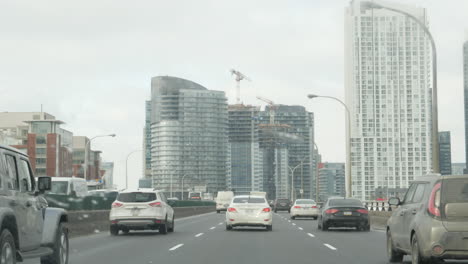 POV-shot-of-using-windshield-wipers-while-driving-on-the-Gardiner-Expressway-in-Toronto,-towards-a-new-condo-building-under-construction