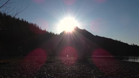 Silhouette-Von-Menschen-Bei-Sonnenuntergang-An-Einem-See-Mit-Bergen-Und-Blendenfleck-Im-Hintergrund