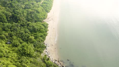 High-aerial-view-of-two-people-walking-on-a-beach,-tropical-coast-on-brazilian-ocean,-Santa-Catarina,-Brazil