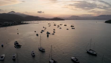Aerial-view-distancing-of-yachts,-boats-and-sailboats-anchored-near-the-coast-at-a-bautiful-sunset