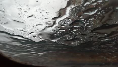 Slow-motion-abstract-view-of-rain-drops-landing-on-glass-as-seen-from-below,-underneath,-gray-sky
