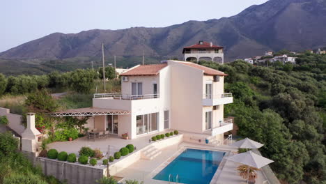Aerial-Counter-Clockwise-Fly-Around-of-Luxury-Greek-Villa-with-Pool-with-Mountains-in-Background-and-Green-Foliage-in-Foreground