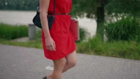 Detail-shot-of-attractive-woman-in-red-dress-walking-on-the-pavement-in-the-park-with-a-laptop-in-her-hand