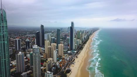 Aerial-moving-back-view-of-skyscraper-city-by-the-beach-with-turquoise-blue-ocean
