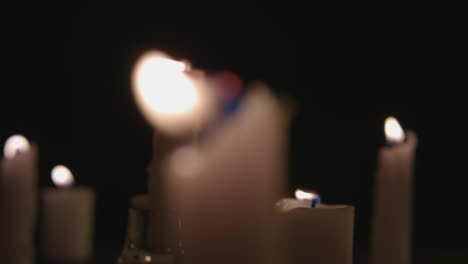 An-extreme-close-up-and-pan-across-of-white-candles-lit-with-a-black-background