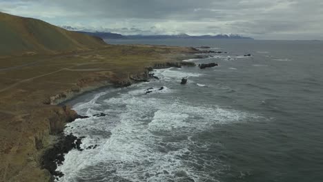Wellen-Krachen-Gegen-Meeresklippen-Mit-Bergkulisse-In-Island