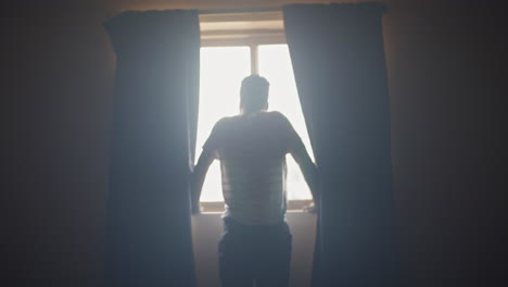 African-American-man-opening-the-curtains-in-a-dark-room-in-the-morning