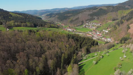 Aerial-view-of-a-small-village-in-a-valley-surrounded-by-hills-and-forest-of-the-blackforest,-Germany