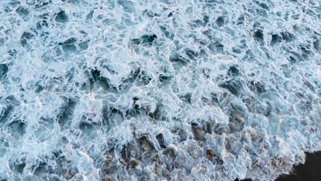 Top-down-shot-of-beautiful-blue-waves-crashing-onto-the-shore-in-Seal-Beach,-CA