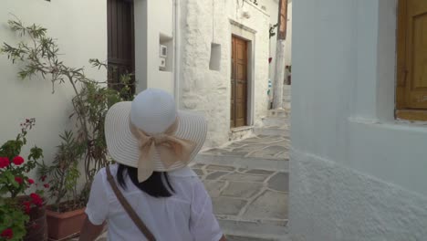 Following-shot-of-girl-in-summery-hiking-outfit-annd-hat-walking-through-typical-narrow-Greek-alley