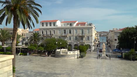 Static-View-of-Syros-Main-square-towards-ocean-with-palm-tree,-greek-flag-and-cars-SLOW-MOTION