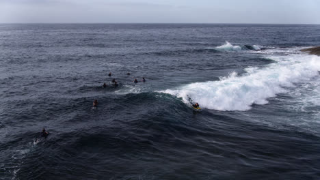 Aerial-tracking-a-group-of-Surfers-and-Bodyboarders-riding-waves-close-to-Rocks