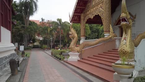 Toma-Panorámica-Lenta-Para-Revelar-La-Impresionante-Entrada-Enmarcada-En-Oro-Del-Templo-Wat-Phra-Singh,-Que-Incluye-Dos-Estatuas-De-Dragones-Míticos-Increíblemente-Detalladas-Y-Un-Joven-Monje