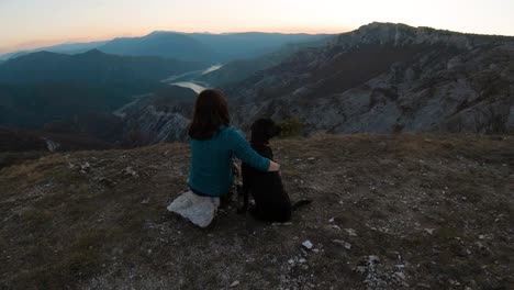 Girl-sitting-and-cudling-black-labrador-dog-on-a-mountain