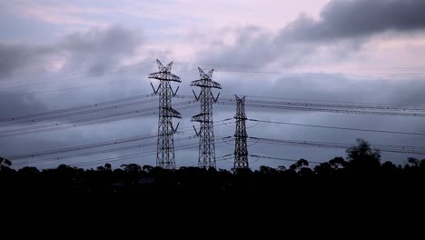 Storm-clouds-rolling-past-electricity-pylons-during-dusk