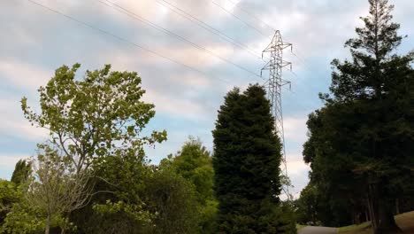 Time-lapse-of-a-high-voltage-power-pylon-tower-rising-high-above-the-trees-on-a-sunny-day