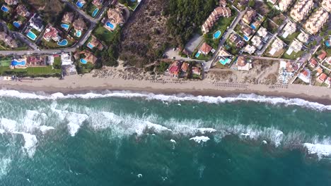 Aerial-view-high-up-looking-down-at-waves-crashing-on-in-on-Spanish-coastline,-summer-beach-view-from-high-in-the-sky-filmed-from-4k-drone