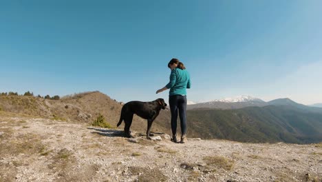 Girl-standing-on-a-mountain-with-black-labrador-dog,-on-a-sunny-autunm-day