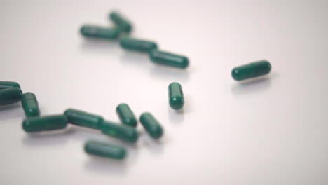 Slow-Motion-Macro-of-Green-Pills-Dropped-onto-White-Background