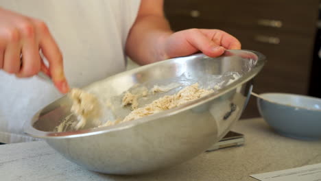 Young-Aspiring-Chef-is-Making-Pizza-Bread-Dough-to-bake,-forming-the-dough-in-a-metal-bowl-with-a-metal-spoon,-a-mix-of-flour,-water-and-egg