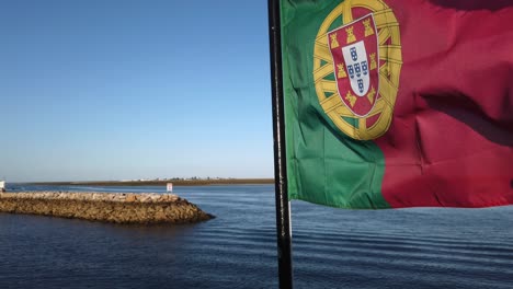 Portuguese-flag-waves-in-foreground,-Olhao-marina-in-background,-Portugal,-extreme-close-up