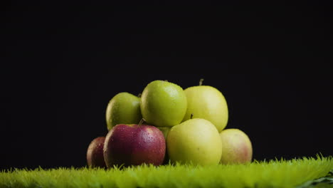 Close-look-of-pile-of-fresh,-shiny-apples-on-rotating-grass-surface-against-black-background