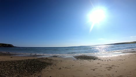 Zwei-Junge-Frauen-Spazieren-An-Einem-Sandstrand-Mit-Sonne-Darüber-Und-Blauem-Meer