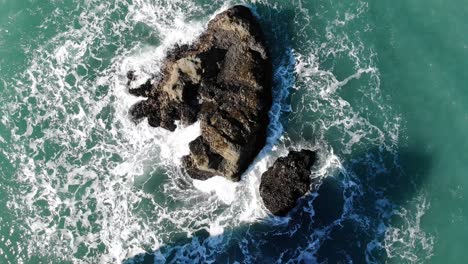 Drone-looks-down-over-sea-stack-as-waves-crash-into-it