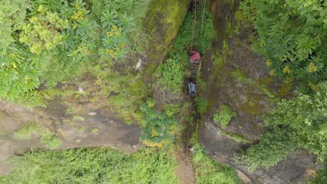 Birds-eye-aerial-shot-of-a-Ugandan-youth-climbing-a-risky-dangerous-ladder-up-the-side-of-a-cliff-in-a-jungle-valley-in-Africa
