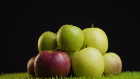 Bunch-of-Green-and-Red-fresh-Apples-on-Grass-against-Black-Background