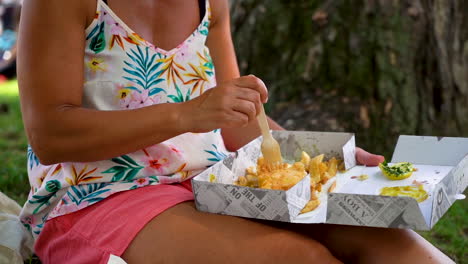 woman-eating-fish-and-chips-out-of-a-box-in-a-park-of-England,-Gloucestershire