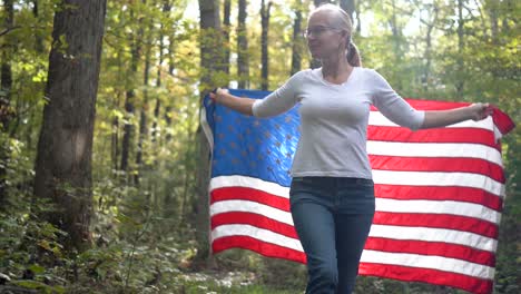 Blonde-woman-looking-up-towards-the-sky-holding-a-flag-behind-her-and-raising-it-as-she-walks-forward-in-a-forest