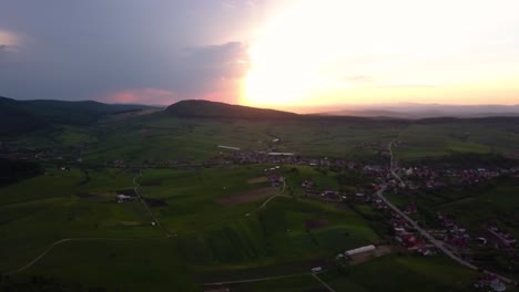 Große-Luftaufnahme-Eines-Tollen-Sonnenuntergangs-über-Weiten-Feldern-Und-Grünen-Wiesen-In-Der-Nähe-Einer-Kehrseite,-Siebenbürgen,-Rumänien