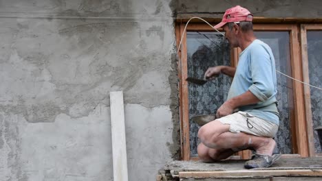 A-hardworking-man-places-cement-on-the-window-ledge-on-the-outside-of-his-house