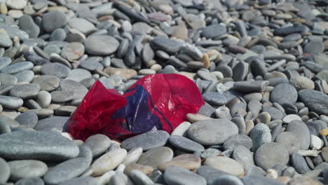 Red-plastic-bag-littering-a-pebble-beach