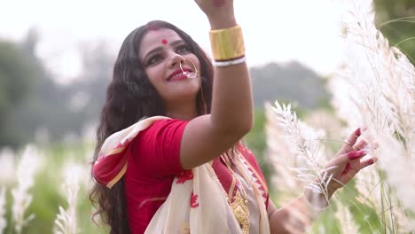 A-playful-and-beautiful-Indian-bengali-married-woman-plays-with-kaash-phool-or-Saccharum-Spontaneum-in-a-field-at-sunset-or-sunrise,-slow-motion