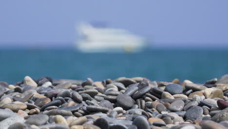Pebbles-on-sunny-beach-with-blurry-ship-at-sea
