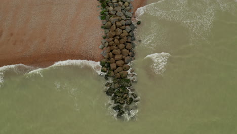 Aerial-top-down-view-of-the-coastline-in-the-south-England-with-a-stone-pile-barrier,-the-shot-is-rising-up-slowly