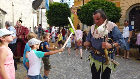 Slow-motion-of-peasant-children-fighting-and-having-fun-with-the-court-jester,-Medieval-reenactment,-Preludij-festival-in-Slovenj-Gradec-slovenia