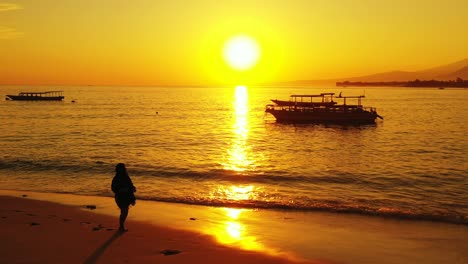 Frau-Macht-Einen-Ruhigen-Und-Entspannenden-Spaziergang-Am-Strand-Der-Bahamas-Mit-Der-Orangefarbenen-Untergehenden-Sonne-Im-Hintergrund-–-Totalaufnahme