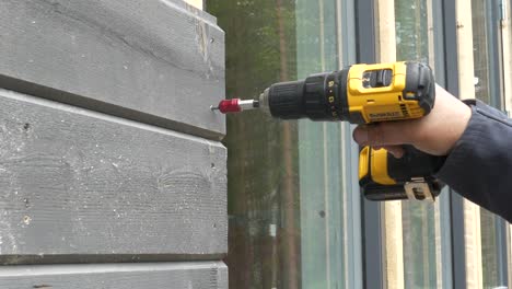 Worker-Tightens-The-Screw-With-A-Screwdriver-In-Wooden-board,-working-on-exterior-facade-of-a-new-house,-static-closeup-shot-in-slow-motion